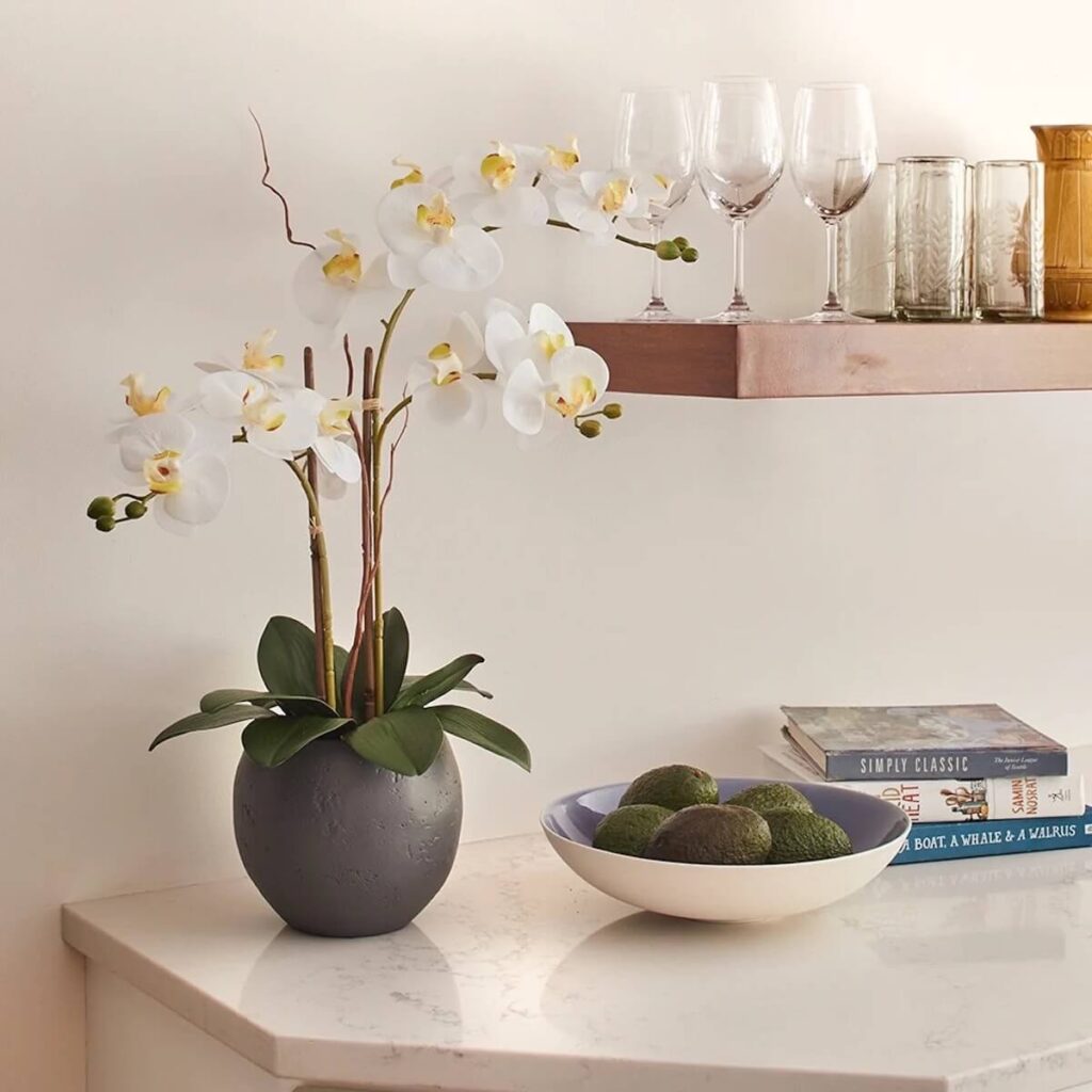 a Ohoto of CG Hunter's three stemmed faux white orchid in a planter, staged in a kitchen on a white counter next to a bowl of avocados.