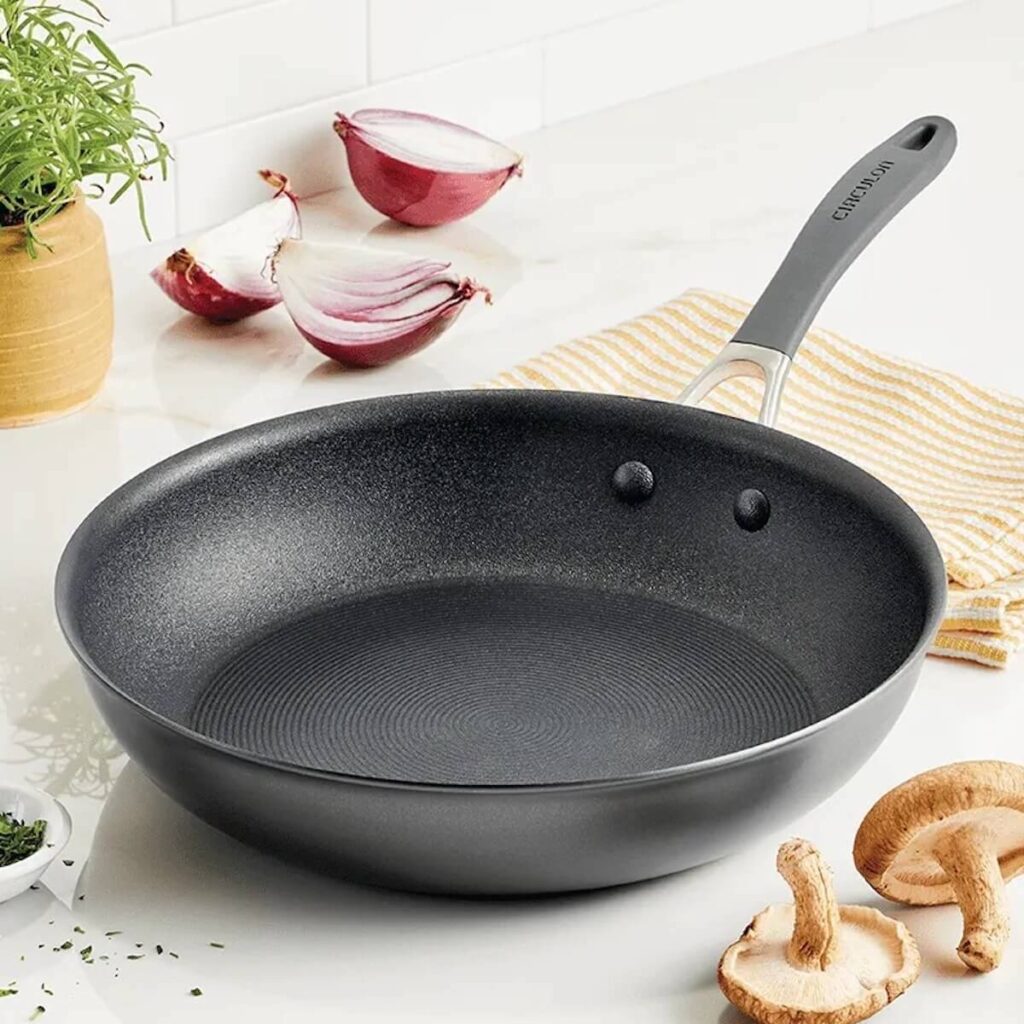 Aluminum, 12 in Circulon nonstick pan with scratch defense sitting on a marble kitchen counter surrounded by fresh cooking produce.