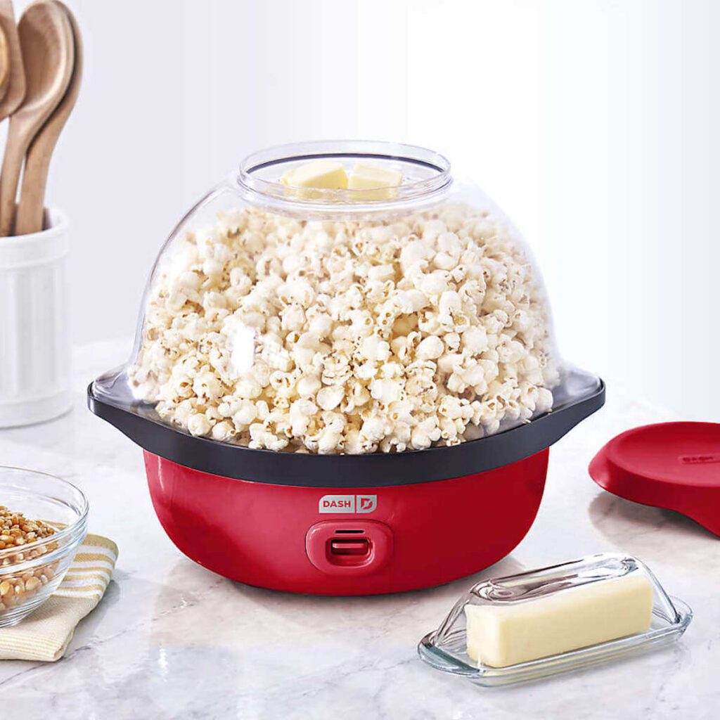 Dash's Smartstore Popcorn maker in red, full of popcorn with two hunks of butter on top.