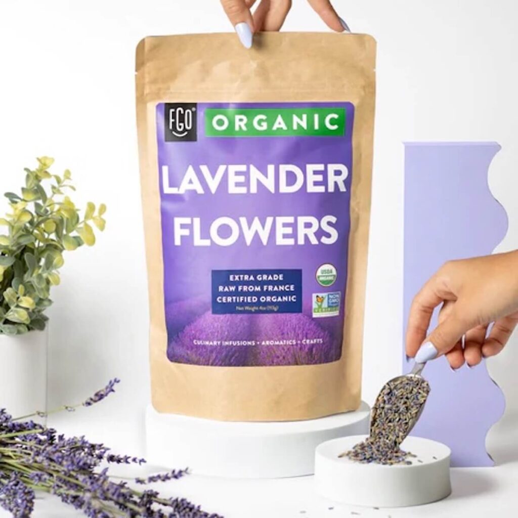 Image of organic lavendar flour buds in their brown paper bag packaging set over a whie background with lavendar flours and the dried buds displayed in front of it.