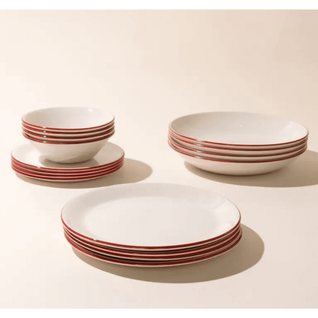 Four plates in four different sizes, cream in color with a red rim , set on a plain cream background.