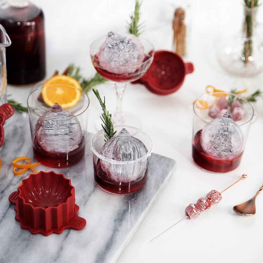 Four ornament shaped, circular ice cubessitting in classes partially filled with a red liquid.