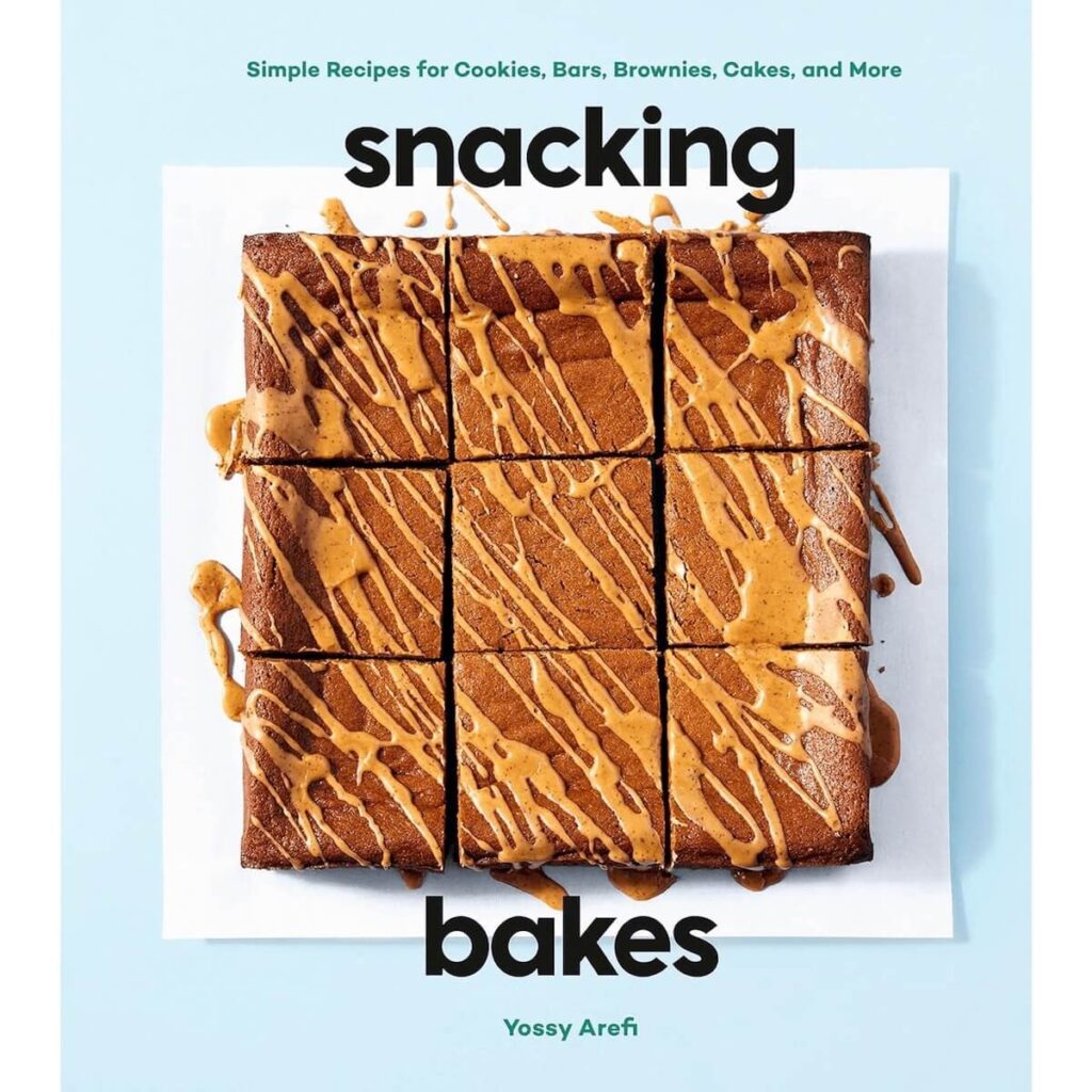 An image of the cover of Snacking Bakes by Yossy Arefi, which is blue with a square of freshly baked chocolate brownies drizzled with a caramel sauce.