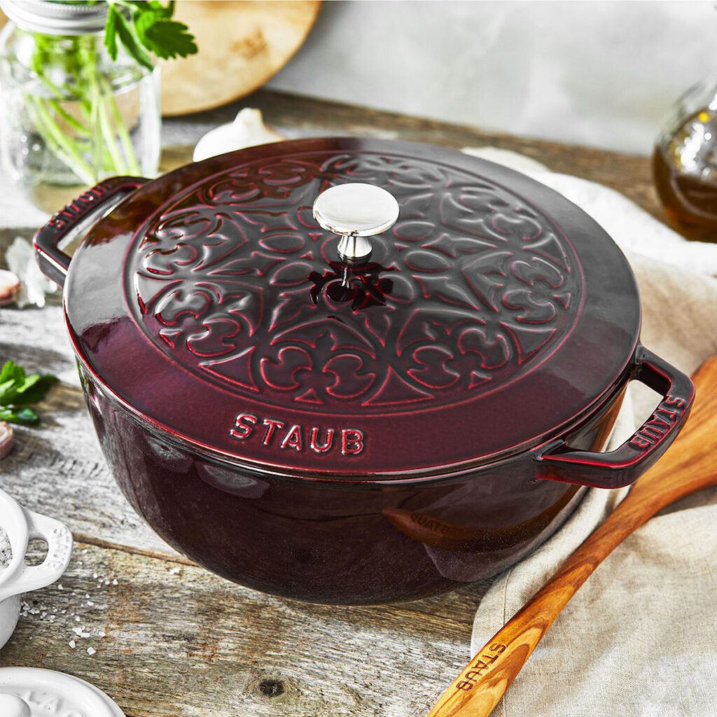 Deep Red Staub dutch oven in a kitchen environment with a lid decorated like a snowflake.