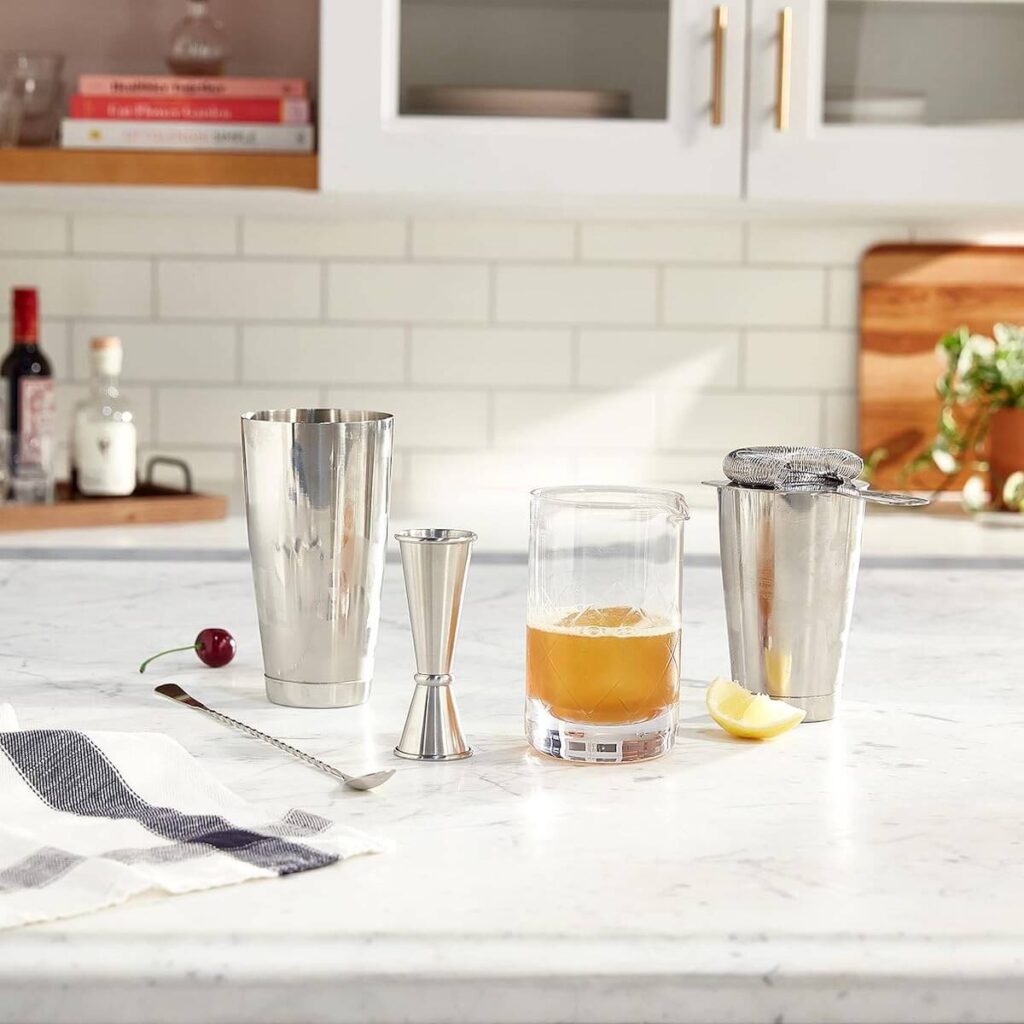 Stainless steel barfly essential mixing cocktail kit including a 17 oz mixing glass, 2oz japanese style jigger, japanese style bar spoon, cocktail shaker/tin set, and heavy duty bar strainer laid out in a light kitchen on a marble counter top.