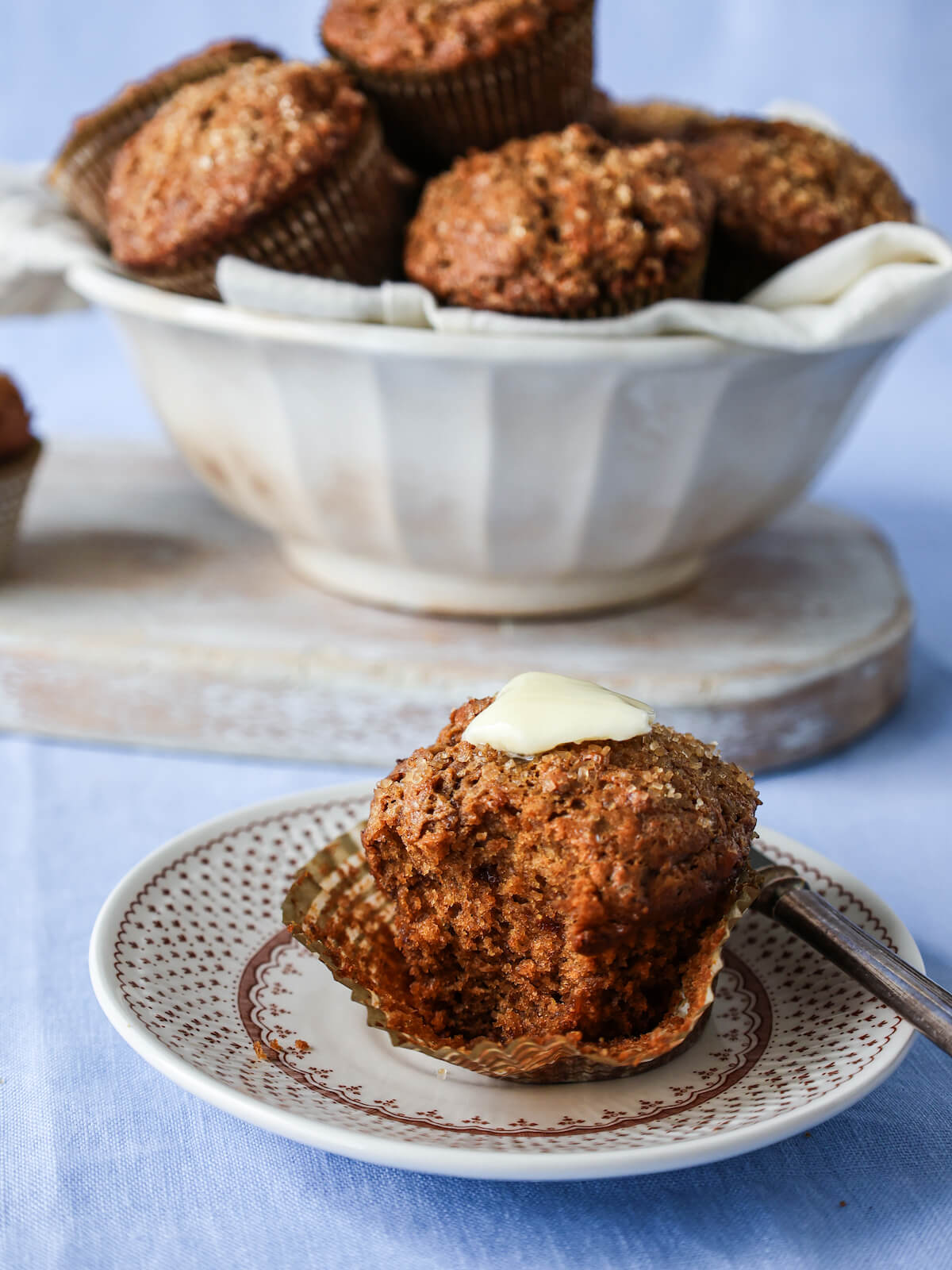 Bran muffin sitting on a plate in front of a bowl of muffins.