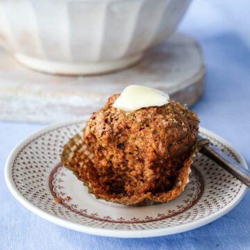 Close up of bran muffin sitting on a plate in front of a bowl of muffins.