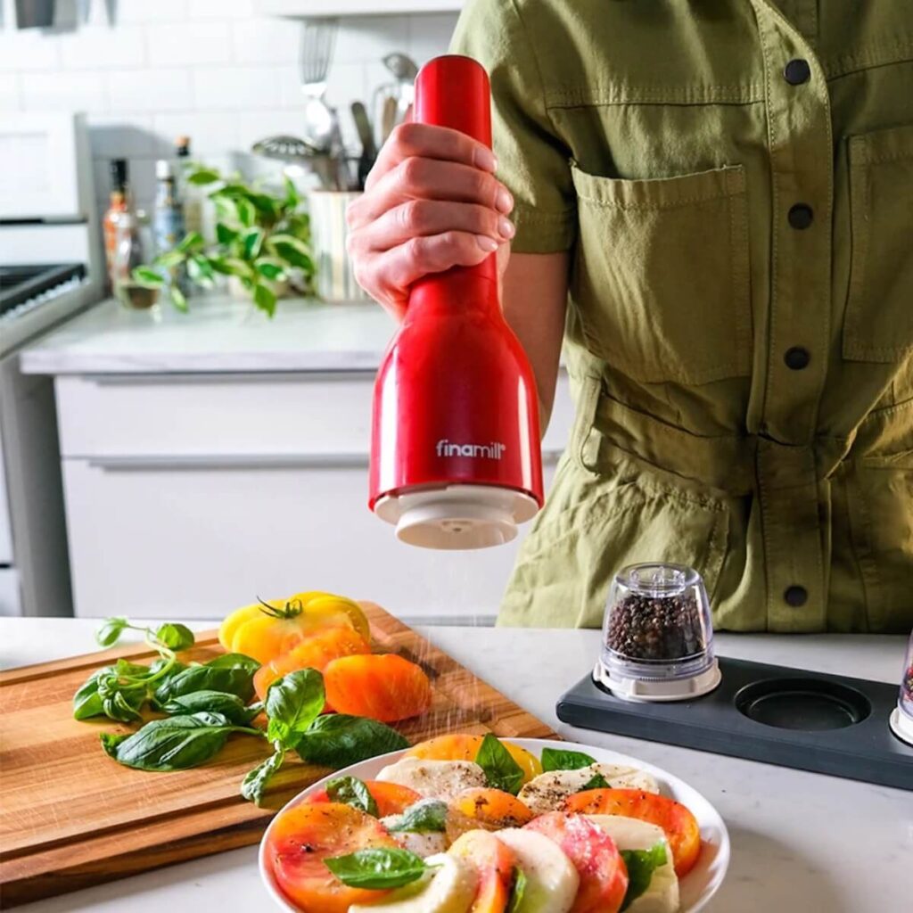 FinaMill's Battery-Operated Pepper & Spice Grinder in the color red, grinding pepper in a kitchen over a place of fresh caprese salad.