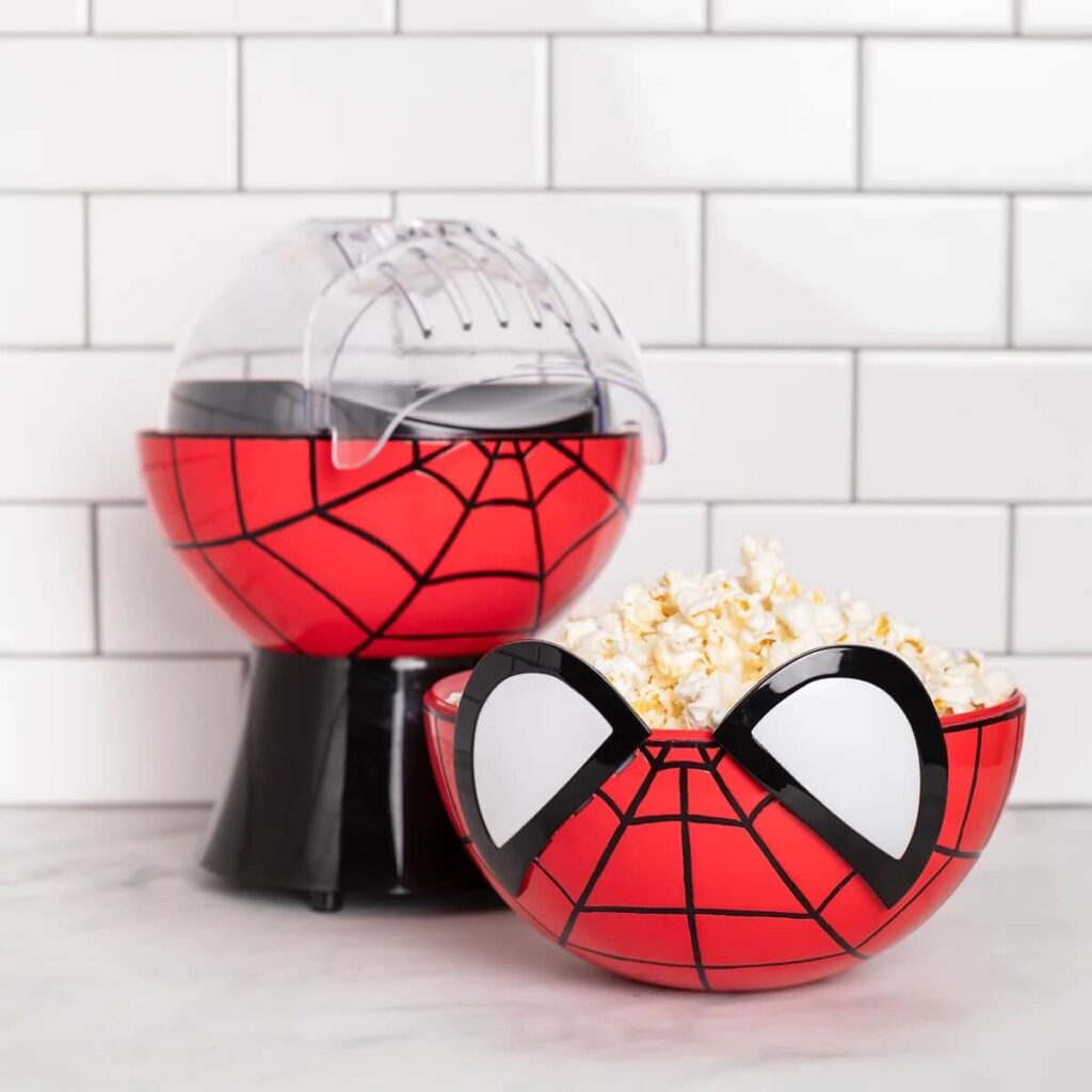 A marvel spider-man popcorn maker in red, with the top portion taken off and filled with popcorn like a bowl, sitting in a white kitchen.