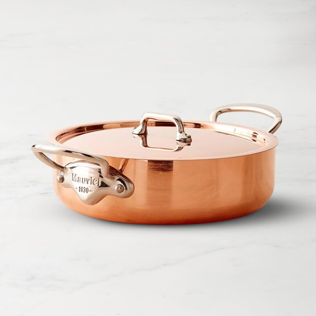 Mauviel's 3.5 quart copper roundeau with a stainless steel interior and bronze handles sitting over a marble background.