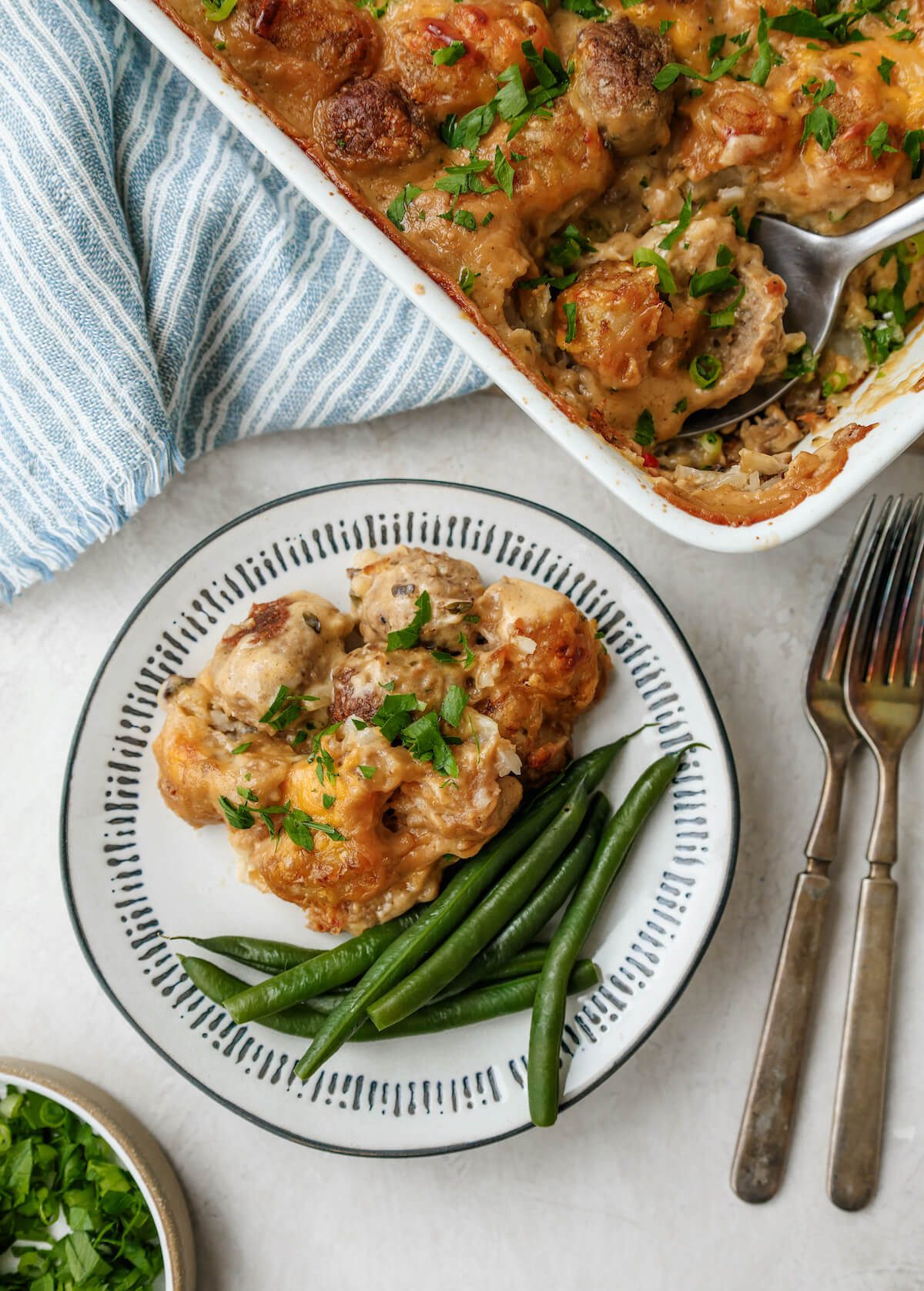 A serving of meatballs and tater tots in cheesy cream sauce with side of green beans.