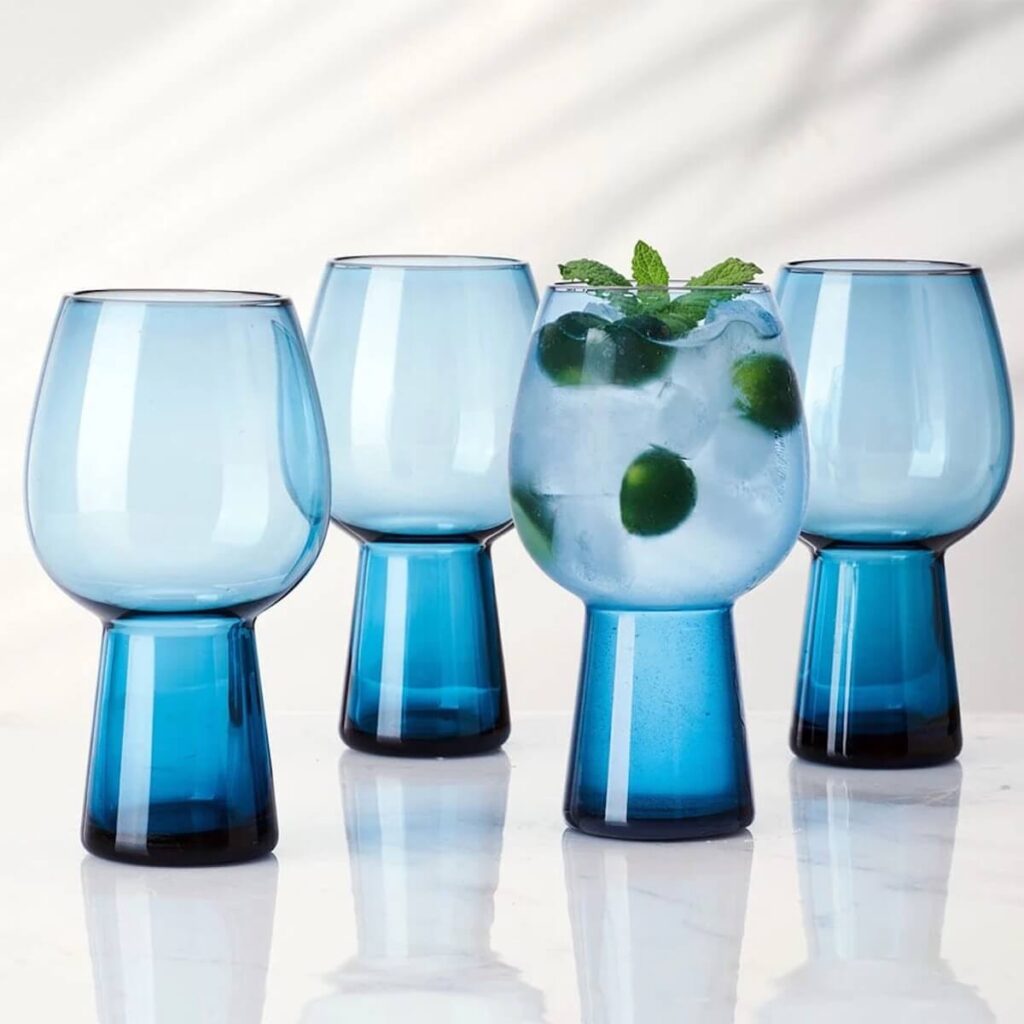 Mikasa's people blue set of 4 beer goblet glasses placed over a white background, one filled with a clear iced drink with olives inside.