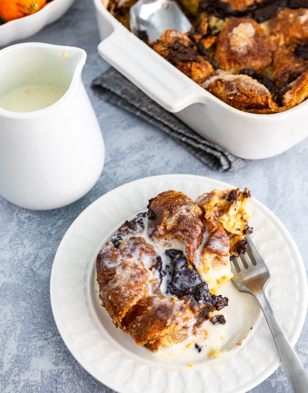 A serving of chocolate croissant bread pudding with orange creme anglaise and a fork with a bite.