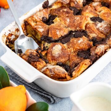 Pan of chocolate croissant bread pudding with a spoon taking a serving out.