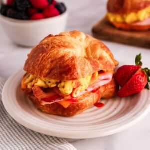 Croissant breakfast sandwich with eggs and breakfast meat, served on a plate with strawberries.