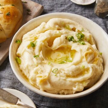 Bowl of mashed potatoes with butter and scallions on a Thanksgiving table.