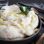 close up of rosemary mashed potatoes in a bowl with fresh rosemary garnish