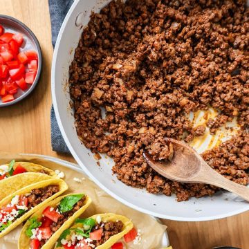 Skillet of beef taco meat on a table ready to serve with hard shell tacos.