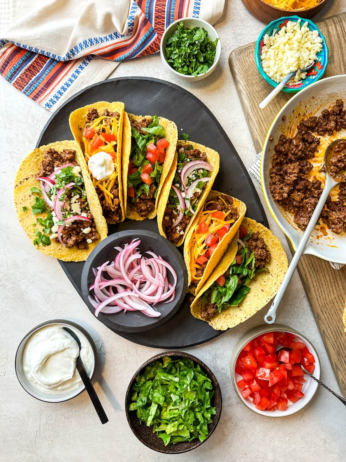 beef tacos on a serving platter with pickled red onions in a bowl and other toppings on the table.