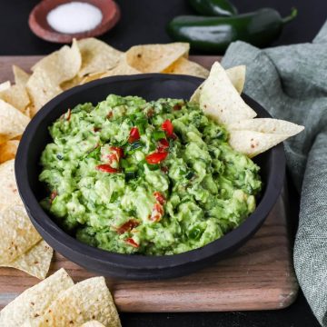 guacamole with jalapenos, scallions, and tomatoes in a black bowl with chips.