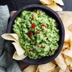 Looking into a bowl of guacamole with classic ingredients and chips.