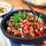 Bowl of pico de gallo salsa with cilantro and a spoon.