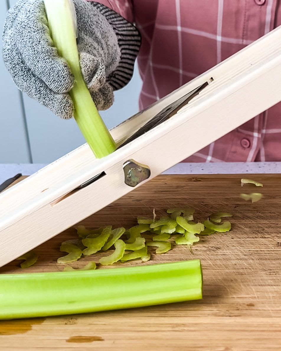 Cutting celery into thin pieces on a mandolin slicer.