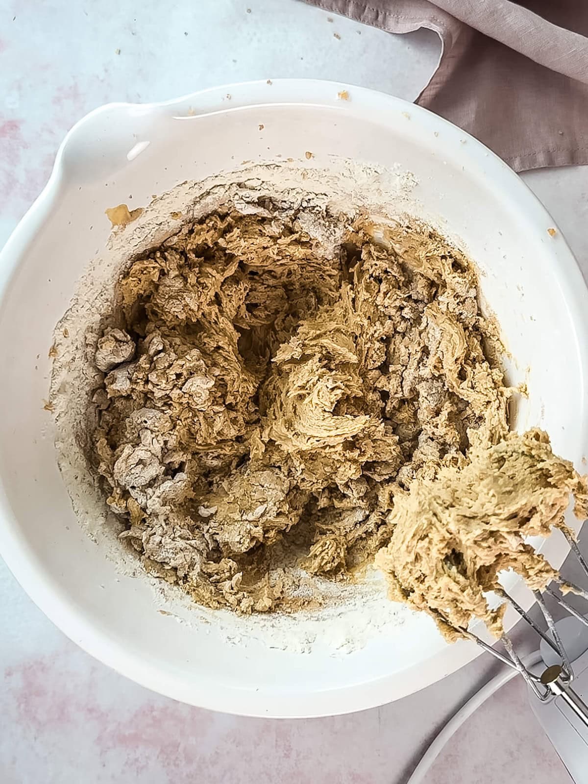 Mixing dry ingredients into the rest of blondie batter in a white mixing bowl.