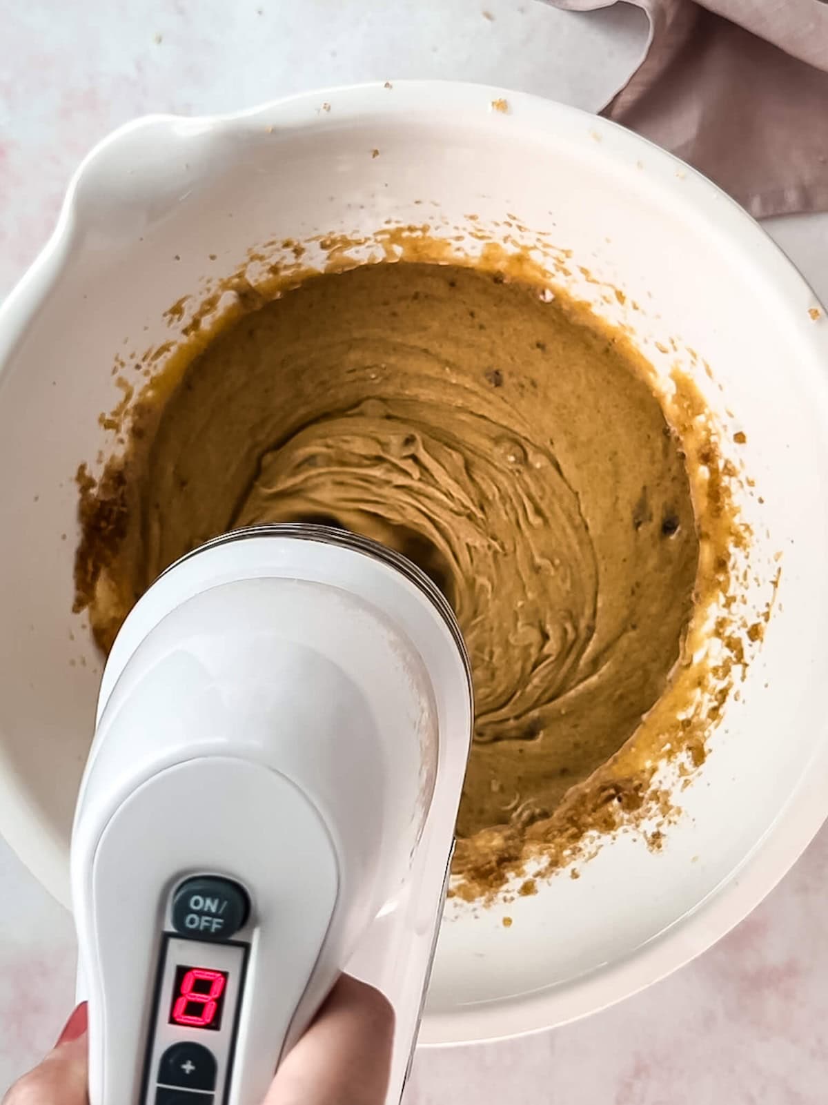 Butter and sugar being creamed in a white mixing bowl.