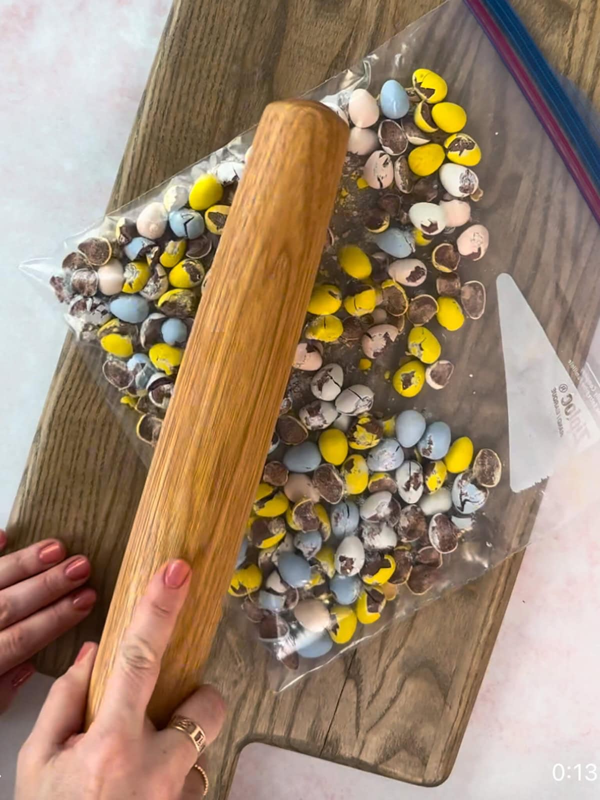 Crushing Cadbury mini eggs in a plastic bag with a rolling pin.