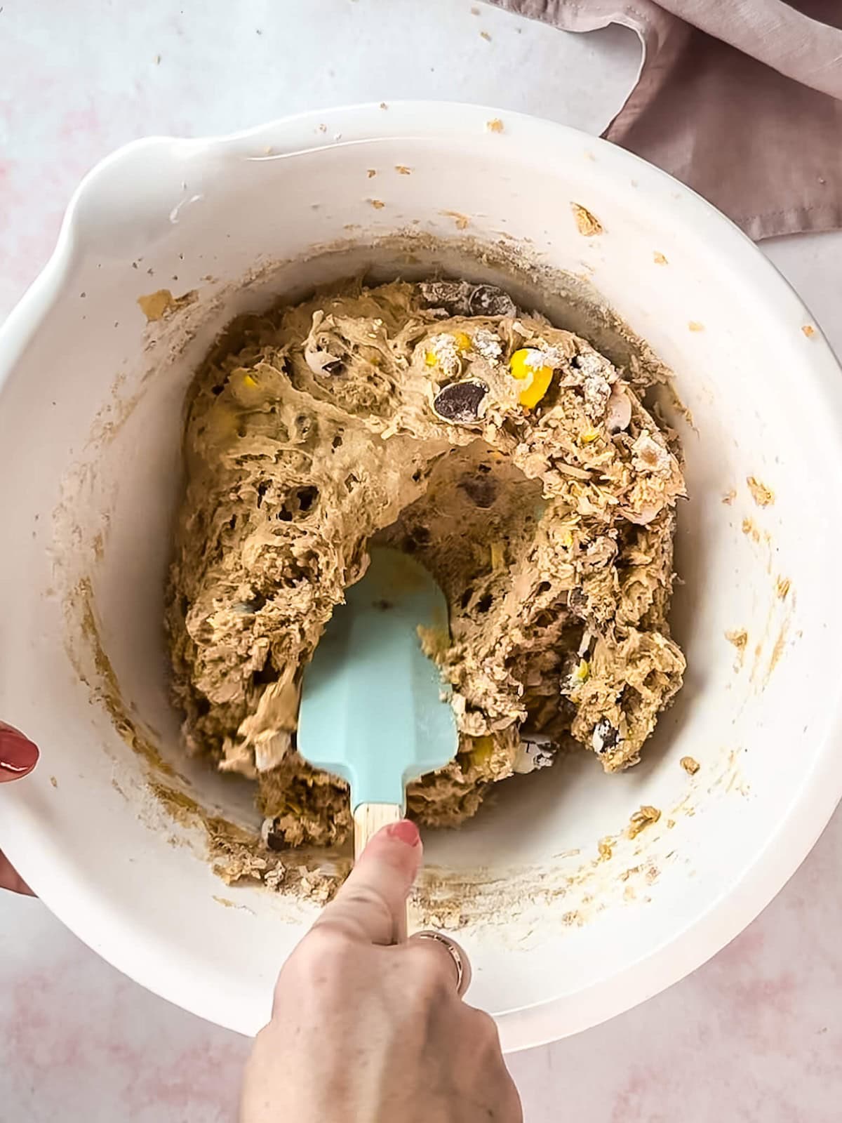 Hand stirring Easter blondie cookie dough in a white mixing bowl.