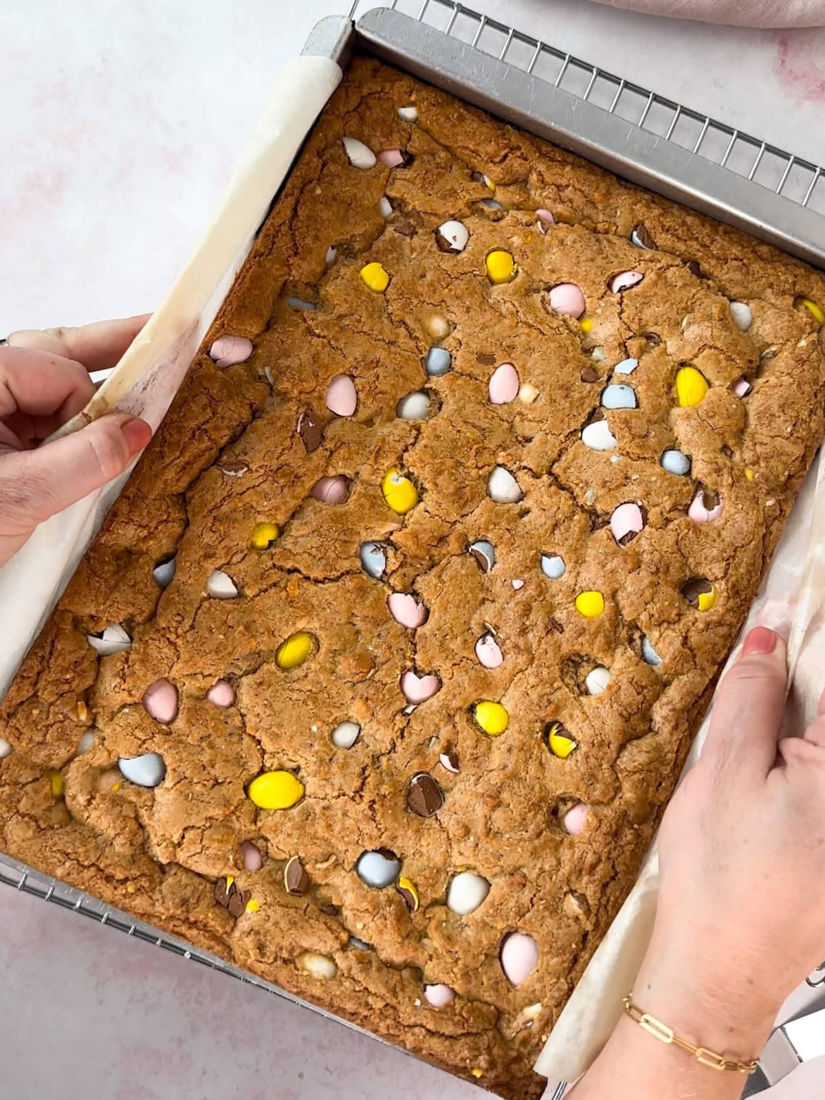 Hands using parchment paper handles to lift baked Easter blondies from pan.