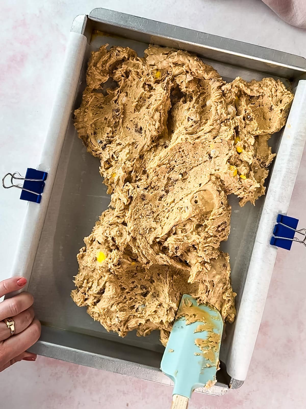 Spatula spreading Easter blondie dough into a prepared baking pan.