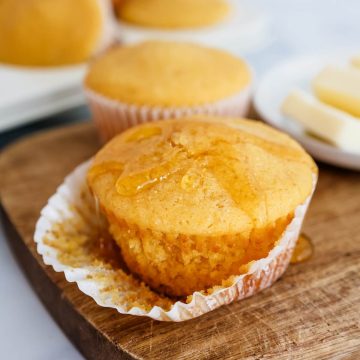 Close up of a partially unwrapped honey cornbread muffin with honey dripping off the top.