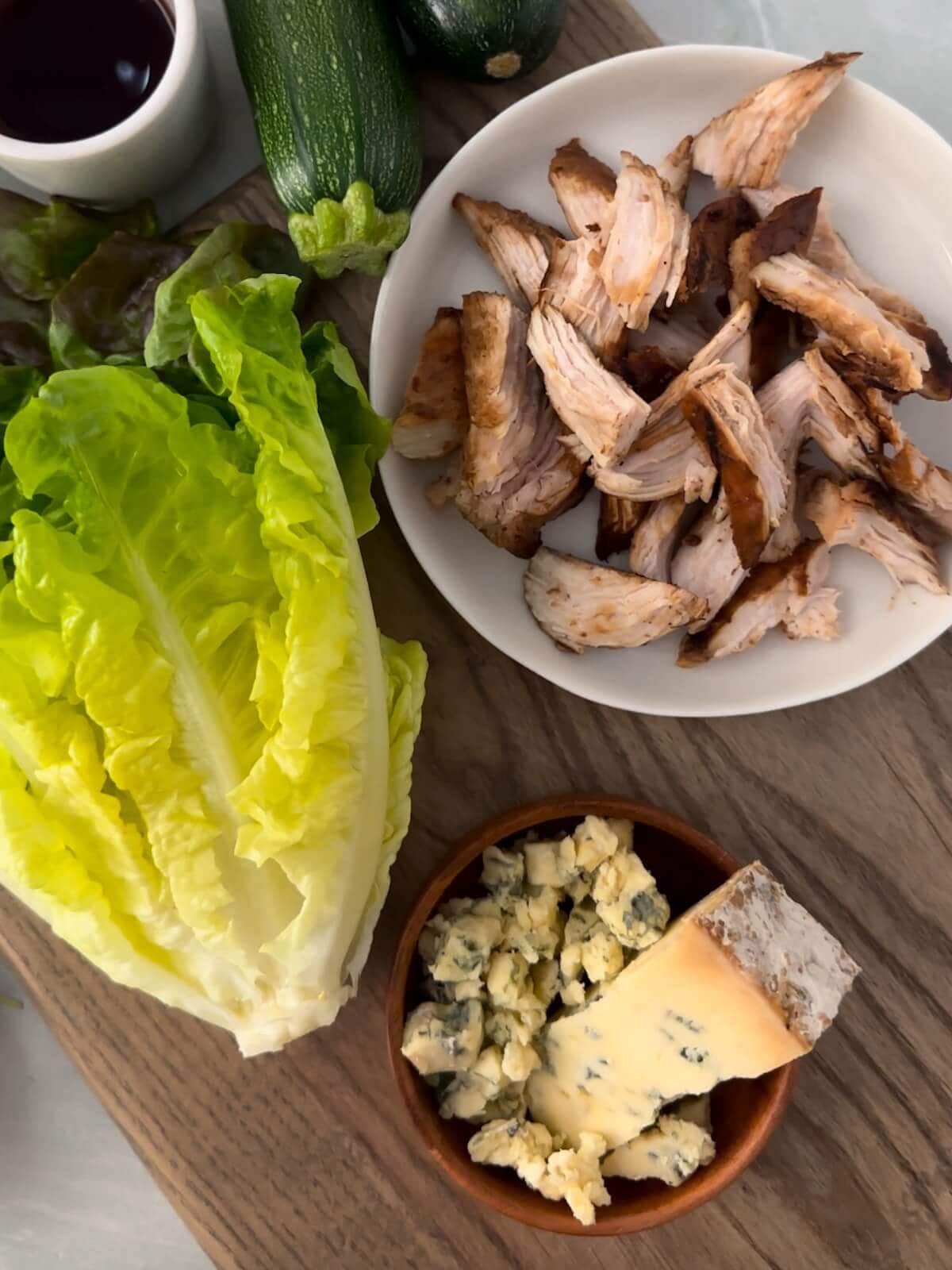 A bowl of shredded chicken, lettuce and crumbled cheese on a cutting board.