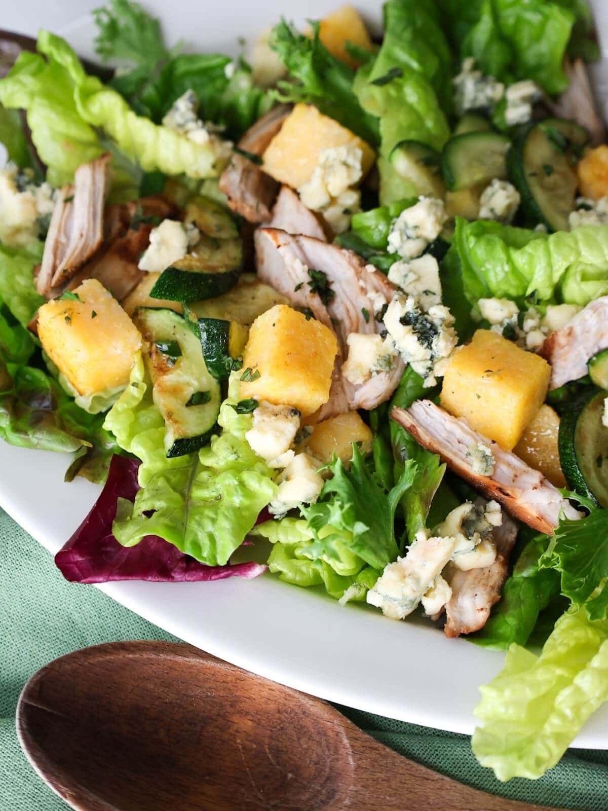 Close up of a polenta zucchini salad next to a wooden spoon.