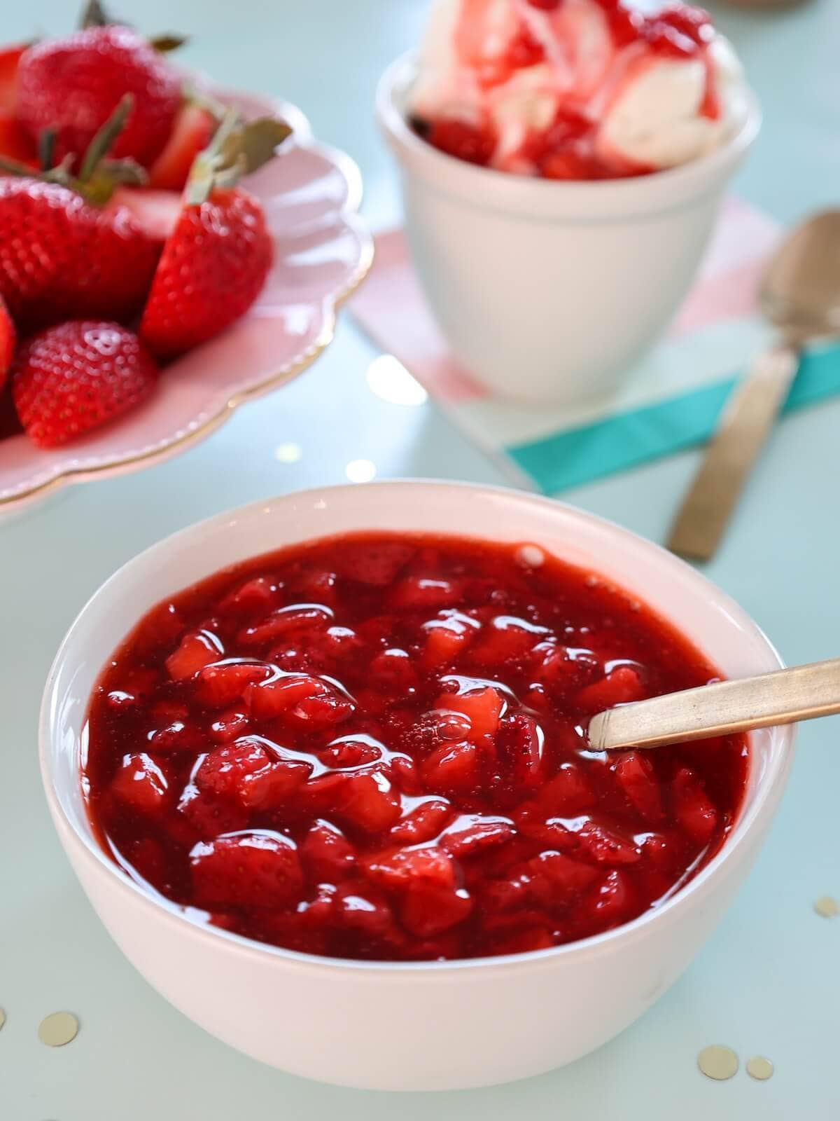 A bowl of strawberry ice cream sauce with strawberries and ice cream in the background.