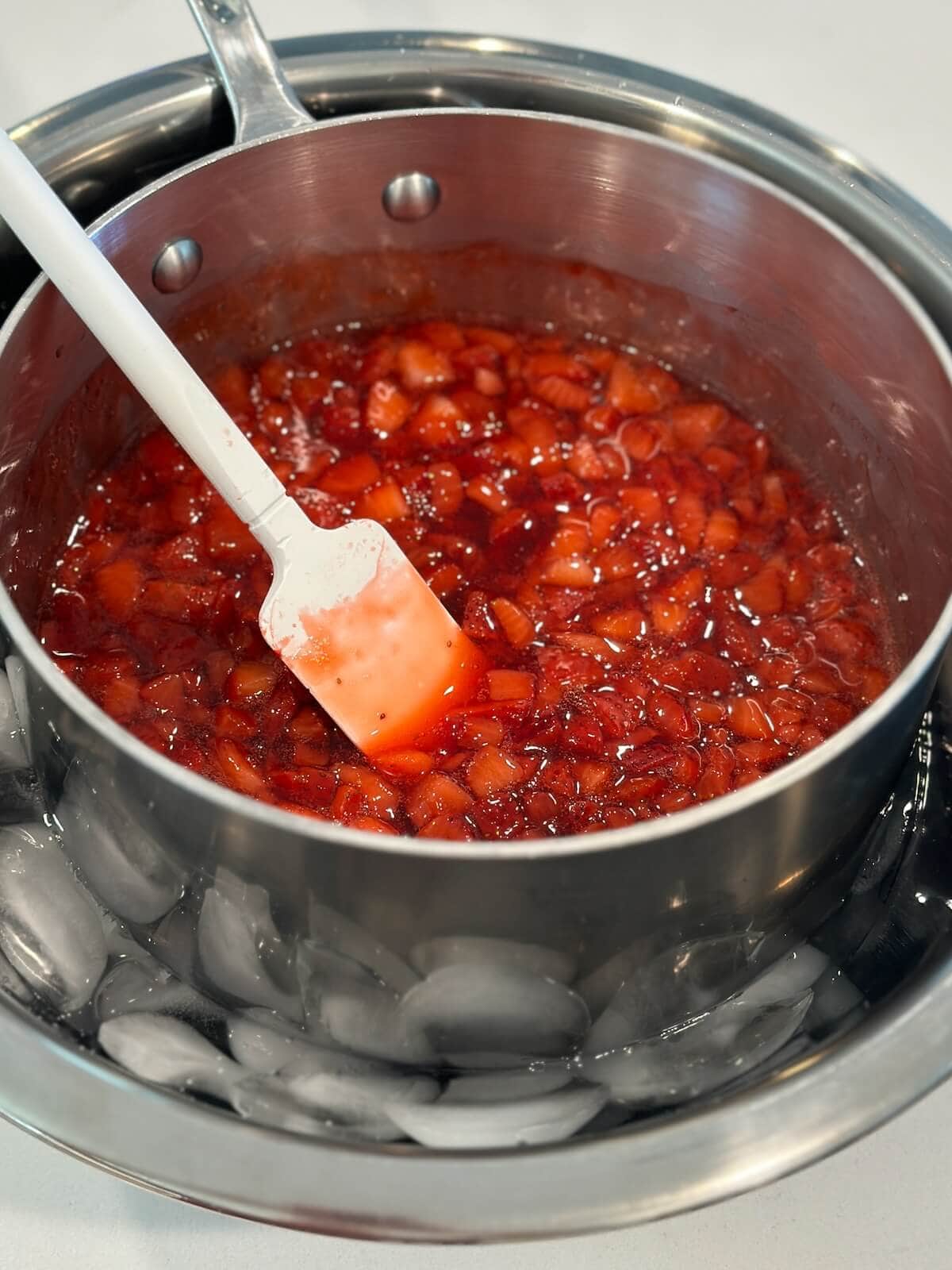 A pot of strawberry ice cream sauce thickening in an ice bath.