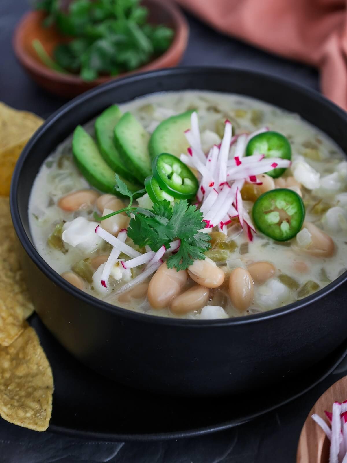 A side view of a bowl of vegetarian white chili with toppings.