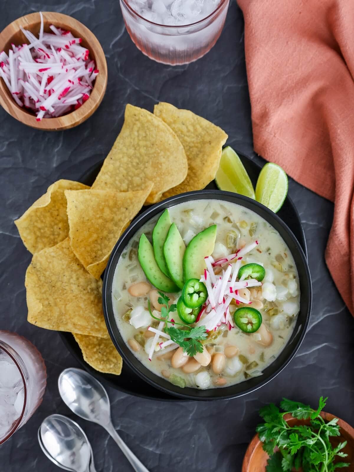 A bowl of vegetarian white chili surrounded by chips and other toppings.