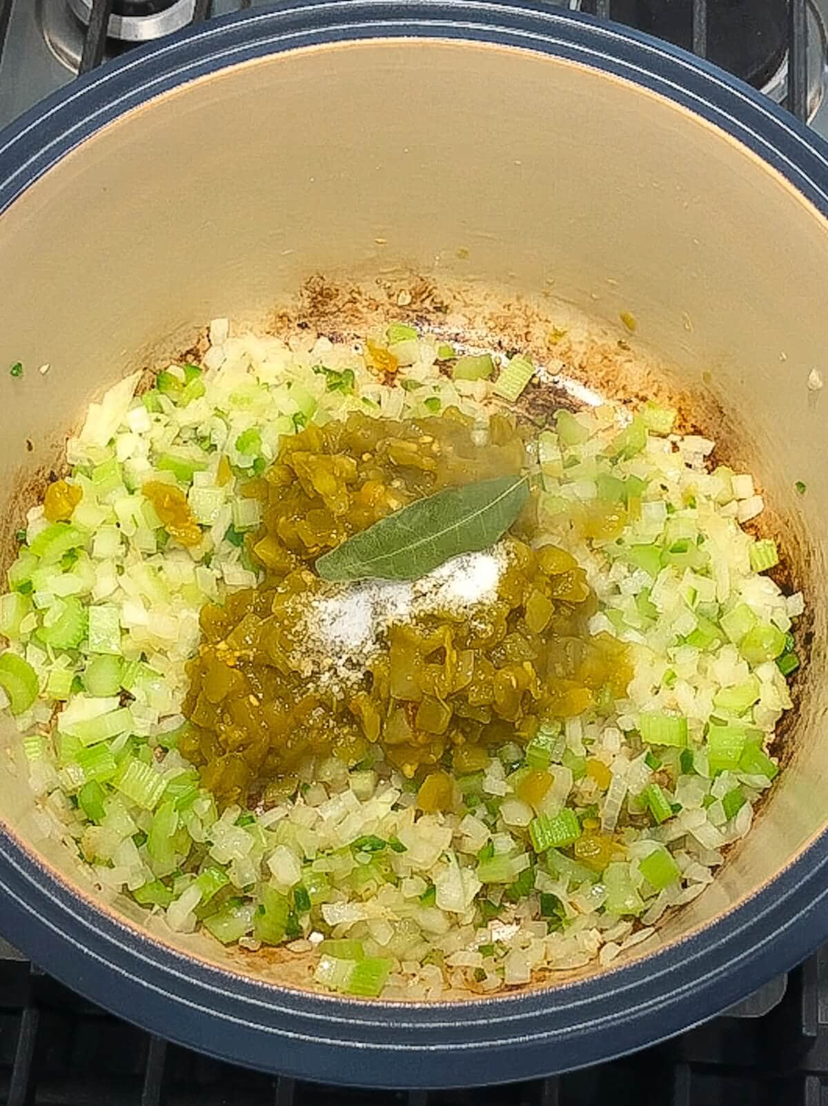 Browned vegetables with roasted chilis and seasonings in the bottom of a pot.