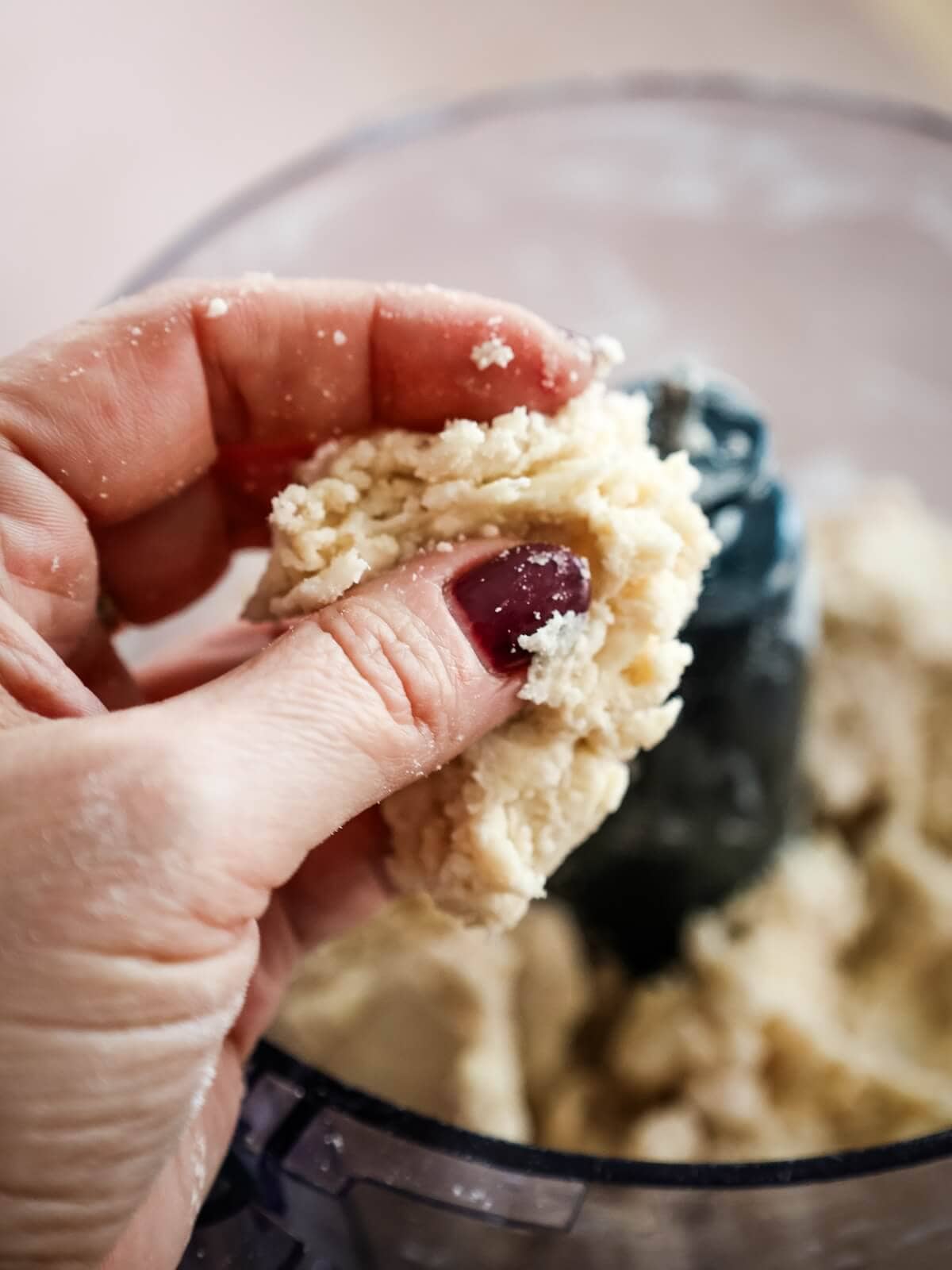 Hand holding a piece of pie crust with food processor in the background.