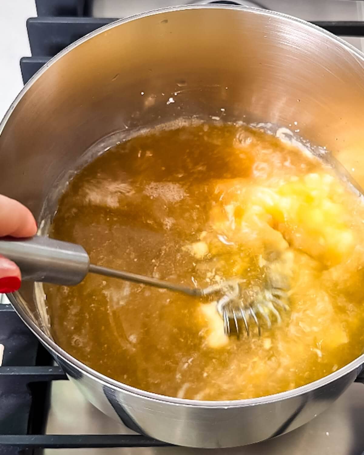 Hand whisking chicken broth into a butter and flour mixture in a saucepan.