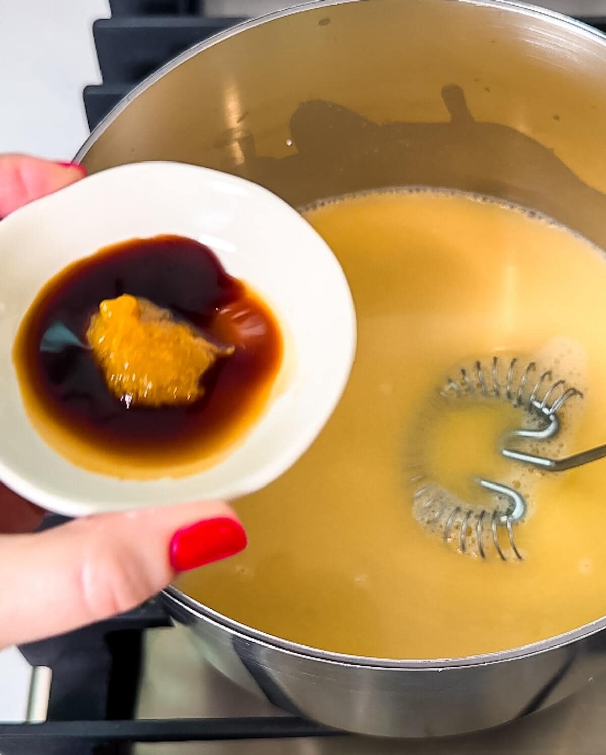 Hand adding Worcestershire and Better Than Bouillon to a gravy base in a saucepan.
