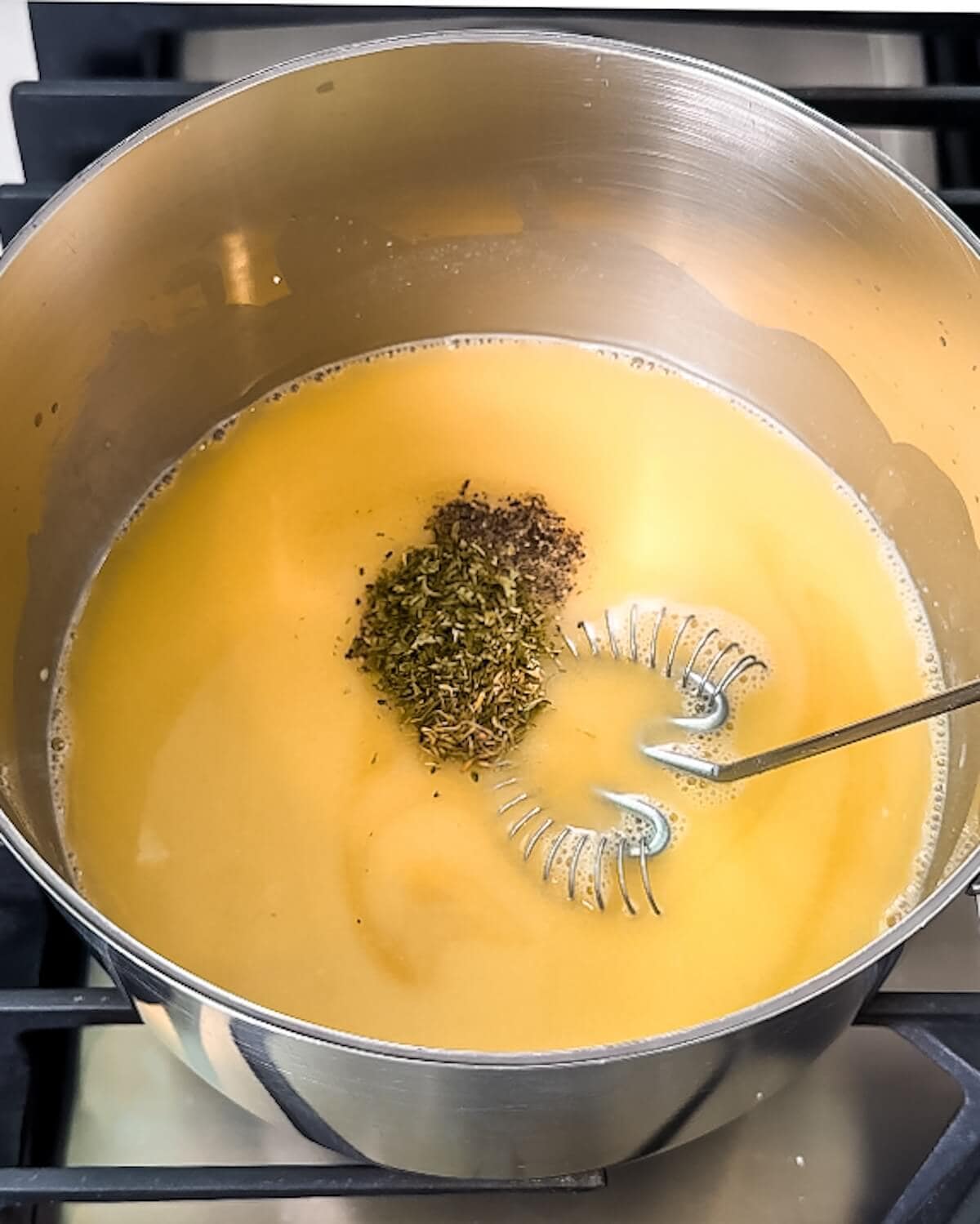 Thyme, parsley, black pepper, and salt being added to a gravy base in a saucepan.