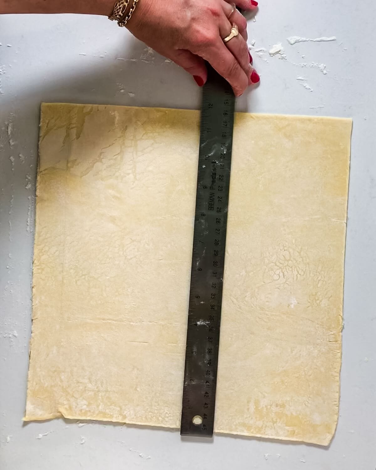 Hand measuring puff pastry with a ruler.