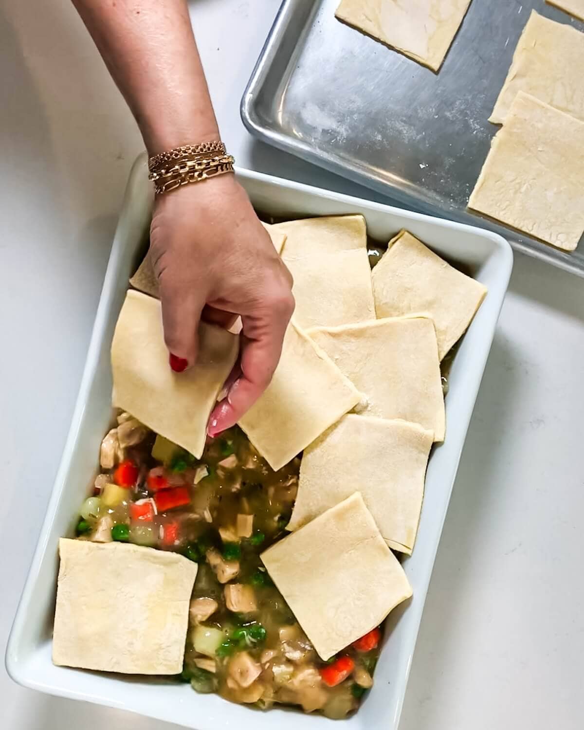 Hand laying puff pastry squares on top of turkey pie filling.