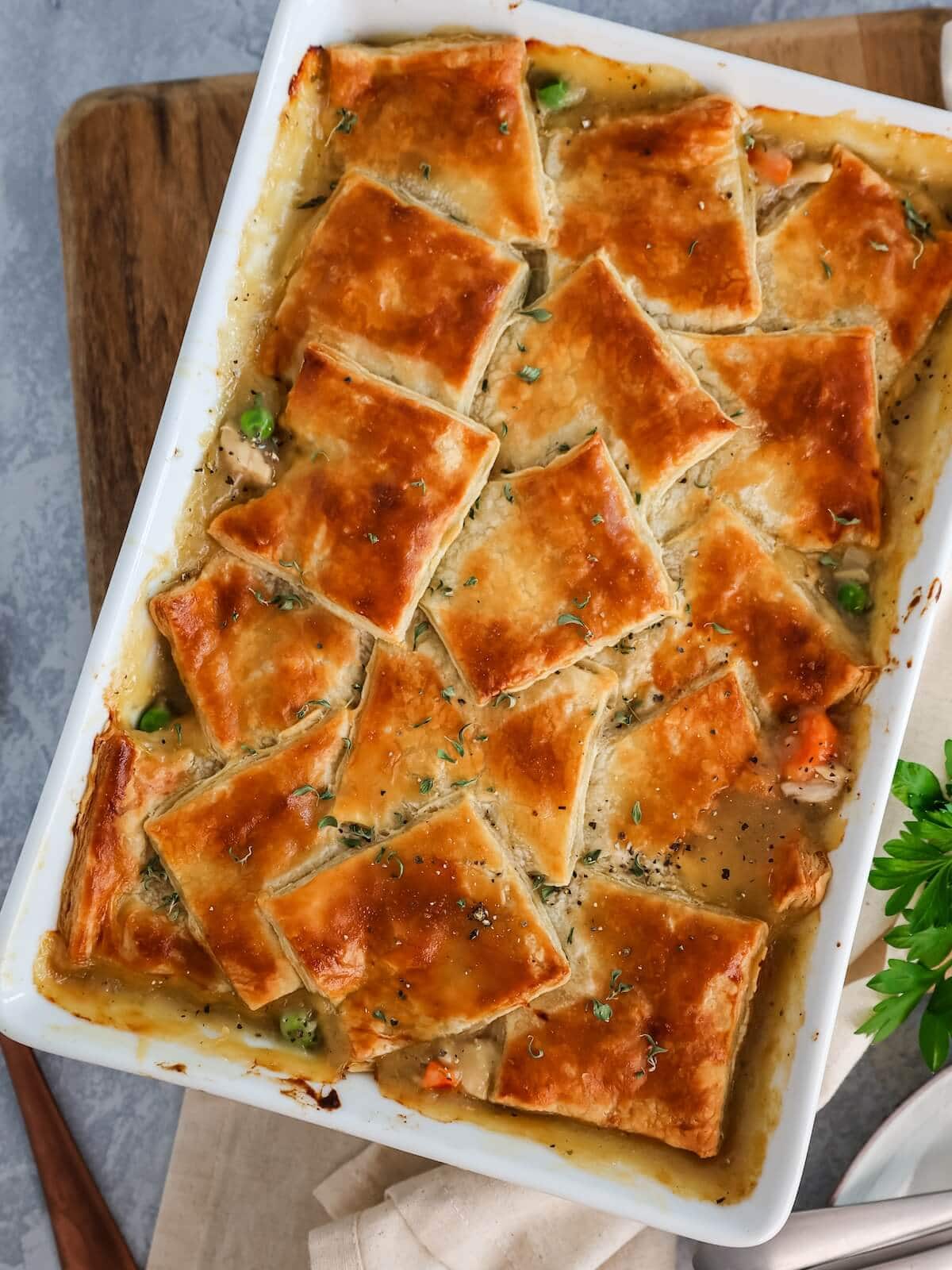 turkey pot pie with puff pastry crust topping baked in a white ceramic dish.