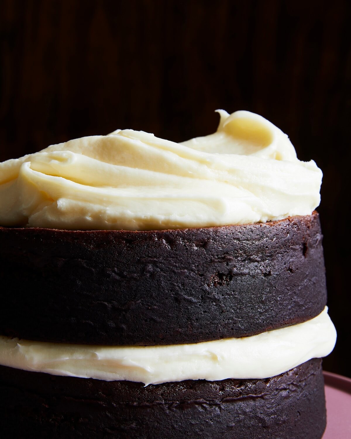 vertical shot of swooped cream cheese frosting on a chocolate cake.