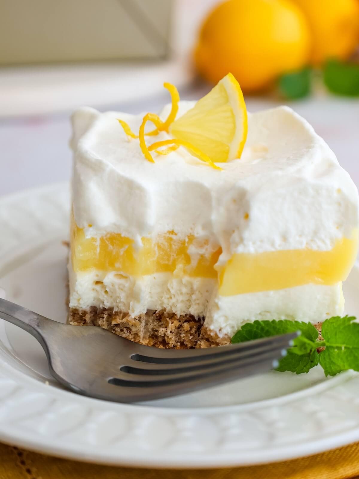 bite out of lemon lush layered dessert on a plate with mint and lemon wedge.